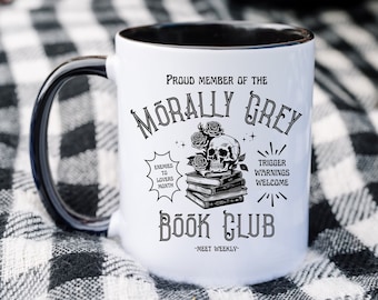 Può includere: Una tazza in ceramica bianca con bordo e manico neri. La tazza presenta un'illustrazione in bianco e nero di uno scheletro con rose, libri e il testo "Morally Grey Book Club - Meet Weekly".