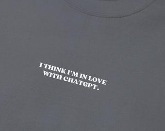 Pode incluir: Uma camiseta cinza escura com o texto "I think I'm in love with ChatGPT." impresso em branco.