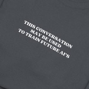 May include: A dark gray t-shirt with the text "THIS CONVERSATION MAY BE USED TO TRAIN FUTURE AI'S" printed in white.