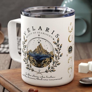 Könnte beinhalten: Weiße Keramik-Reisebecher mit goldenem Design, das eine Bergkette, Sterne und den Text "Velaris, City of Starlight" zeigt. Der Text "To the stars who listen, all the dreams that are answered" ist ebenfalls enthalten.