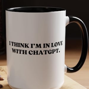 May include: White ceramic mug with a black rim and handle. The mug has black text that reads "I think I'm in love with ChatGPT."