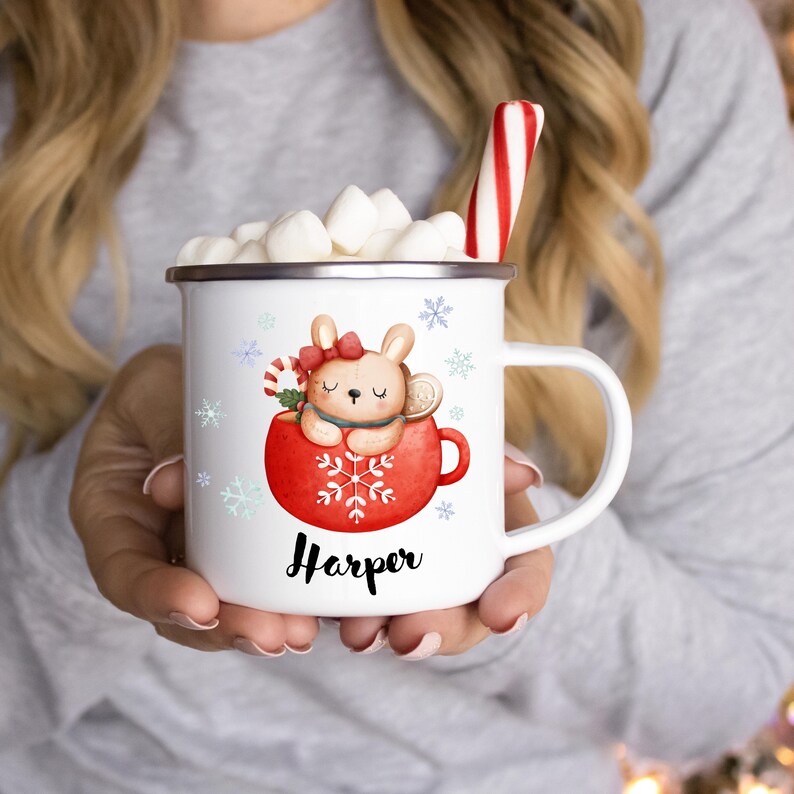 May include: White enamel mug with a red and white illustration of a bunny in a mug with a snowflake design. The mug has the name "Harper" printed on the front.