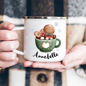 May include: White enamel mug with a green mug with a gingerbread man inside, holding a candy cane. The mug has a heart on the side and the text "Annabelle" is printed below the mug.