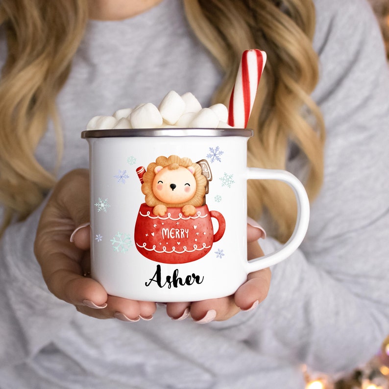 May include: White ceramic mug with a red and white illustration of a lion in a mug with the text "Merry" and the name "Asher". The mug is filled with marshmallows and a red and white candy cane.
