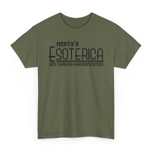 Peut inclure: T-shirt vert olive avec l'inscription noire "Misty's Esoterica and Chakra Harmonization". Le t-shirt a des manches courtes et un col rond. Le texte est centr&eacute; sur le devant du t-shirt.