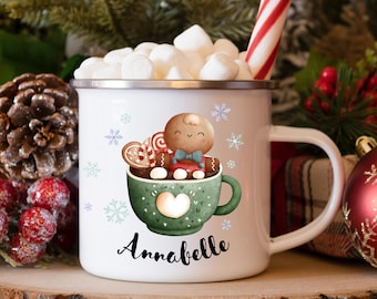 Könnte beinhalten: Weiße Email Tasse mit einem Lebkuchenmann-Design. Der Lebkuchenmann sitzt in einer grünen Tasse mit Marshmallows und Zuckerstangen. Die Tasse trägt den Namen "Annabelle".