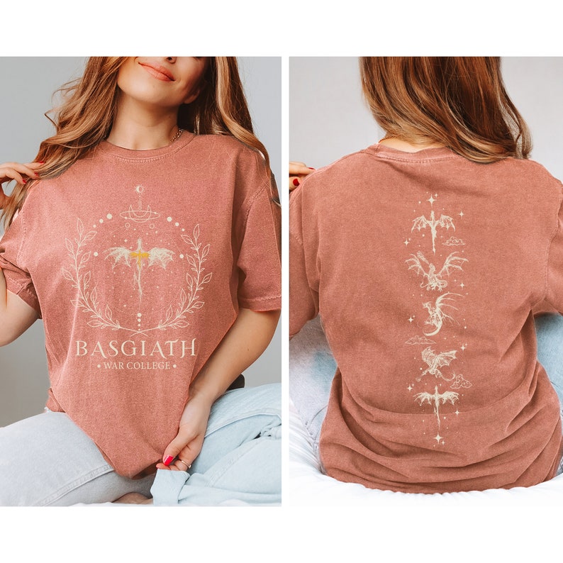 Puede incluir: Una camiseta de color &oacute;xido con un gr&aacute;fico blanco de un drag&oacute;n y el texto "BASGIATH WAR COLLEGE" en la parte delantera. La parte posterior de la camiseta presenta un dise&ntilde;o vertical de cinco dragones.