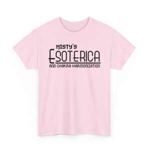 Peut inclure: T-shirt rose clair avec l'inscription noire "Misty's Esoterica and Chakra Harmonization". Le t-shirt est &agrave; manches courtes et col rond.