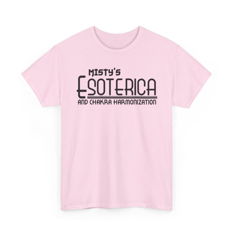 Peut inclure: T-shirt rose clair avec l'inscription noire "Misty's Esoterica and Chakra Harmonization". Le t-shirt est &agrave; manches courtes et col rond.