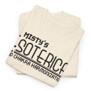 Peut inclure: Deux t-shirts cr&egrave;me sont pli&eacute;s et empil&eacute;s. Le t-shirt sup&eacute;rieur porte l'inscription "Misty's Soteric" en gras noir, avec les mots "and Chakra Harmonization" en dessous. Les t-shirts sont faits d'une mati&egrave;re douce et confortable.