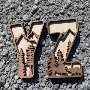 May include: Two wooden letters Y and Z featuring a layered design. The dark brown outer frame contains a light tan wood inlay depicting a mountain range, evergreen trees, and a bear silhouette within the letter Z, creating a dimensional effect.
