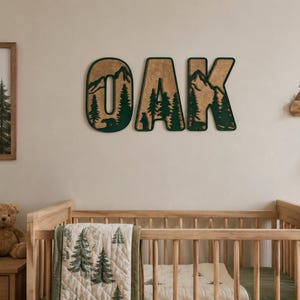 May include: Three large wooden wall letters spelling OAK, featuring a layered design with a natural wood grain finish and a dark green forest silhouette cutout. Each letter displays a detailed mountain landscape with pine trees and a bear.