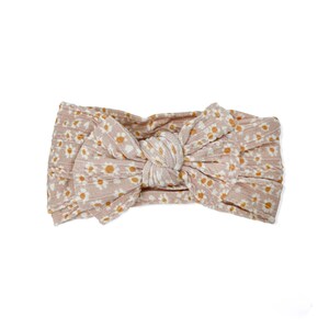 May include: A pink and white knotted headband with a daisy print.