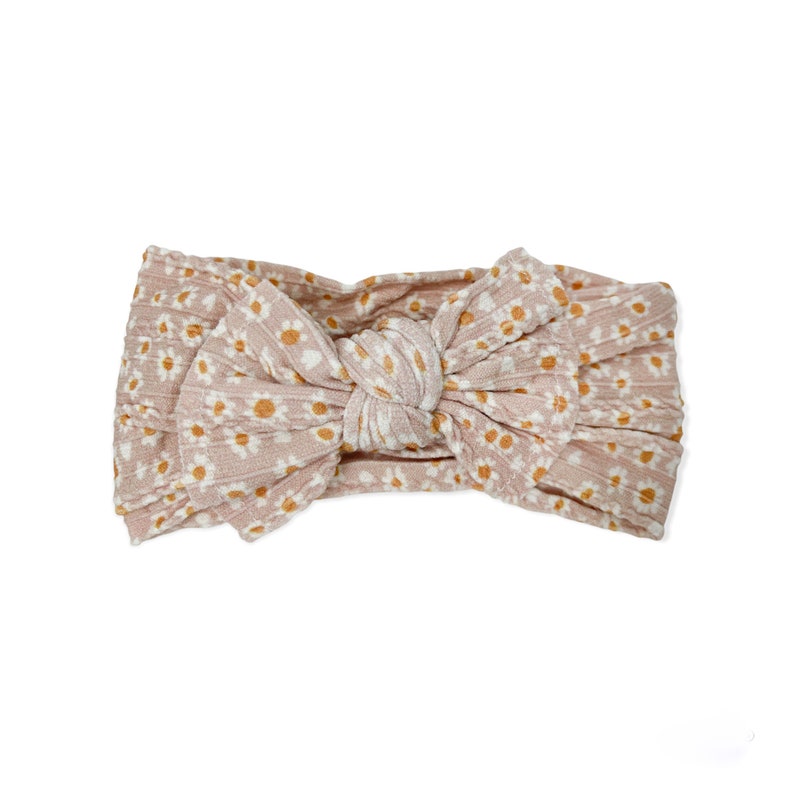 May include: A pink and white knotted headband with a daisy print.