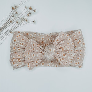 May include: A light brown headband with a knotted bow and a white daisy print.