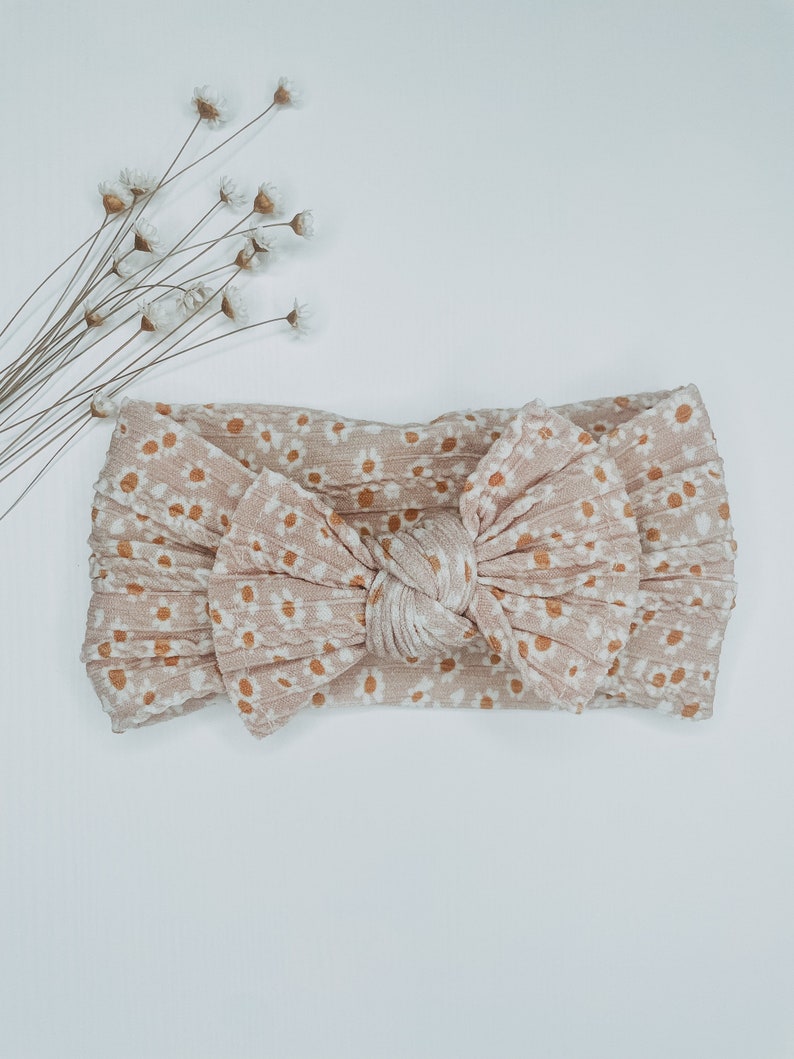 May include: A light brown headband with a knotted bow and a white daisy print.