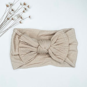 May include: A beige knotted headband with a cable knit texture.