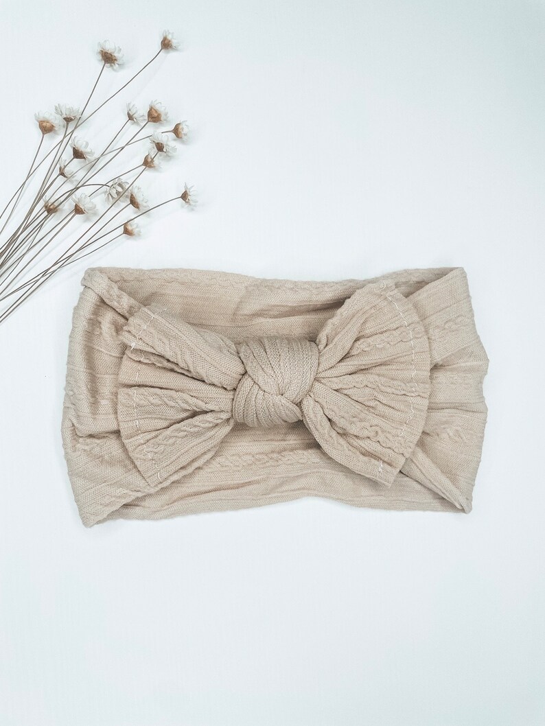 May include: A beige knotted headband with a cable knit texture.