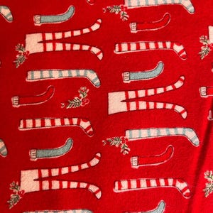 May include: A festive red fabric featuring a repeating pattern of Christmas candy canes, gift boxes, and holly sprigs. The candy canes are white with red stripes and light blue accents. The overall design evokes a holiday theme.