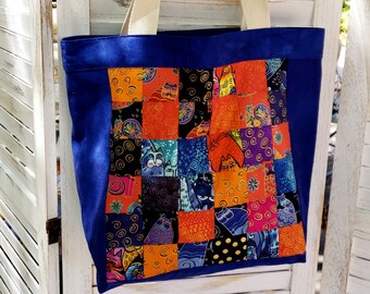 Puede incluir: Una bolsa de lona azul con un diseño de patchwork que presenta gatos coloridos. El patchwork está hecho de cuadrados de diferentes telas con varios patrones y colores, incluyendo naranja, rojo, amarillo, verde, azul y morado. La bolsa tiene dos correas largas de color crema.