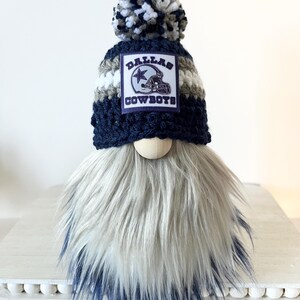May include: A crocheted gnome with a blue and white pom-pom hat. The hat has a white and gray striped band and a patch that says "Dallas Cowboys". The gnome has a long, white and blue beard.