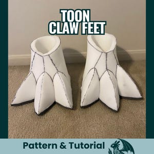 Op de afbeelding: Een paar witte schuimrubberen klauwvoeten met zwarte randen, ontworpen om op cartoonvoeten te lijken. De tekst "TOON CLAW FEET" staat boven de voeten. De voeten staan op een tapijtoppervlak.