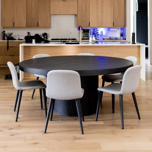 Puede incluir: Una mesa redonda negra con seis sillas tapizadas grises. La mesa está en una cocina moderna con armarios de madera y una encimera blanca.