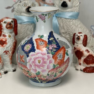 May include: A white porcelain vase with a round body and a narrow neck. The vase is decorated with a floral pattern in shades of pink, red, blue, and green. The flowers are surrounded by leaves and branches.