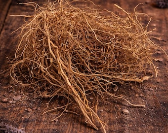 May include: A close-up shot of a pile of dried, light brown roots. The roots are tangled and textured, with some thicker strands and many thin, hair-like fibers. The background is a dark, rustic wooden surface with small pieces of debris.