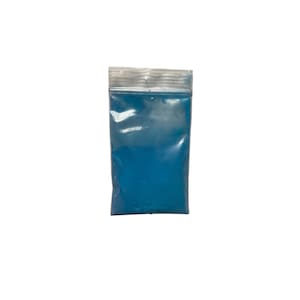 May include: A small, transparent plastic bag containing a vivid blue powder. The bag features a zip-top seal and is presented against a plain white backdrop. The powder looks finely ground and uniformly dispersed inside the bag.