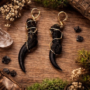 May include: A white ceramic mug with a black handle and the text "But First, Coffee" in a bold, black font. The mug is set against a blurred background, suggesting a cozy setting.