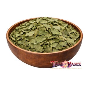 Puede incluir: Un cuenco de madera lleno de hojas verdes secas. El cuenco es de color marrón cálido y tiene un acabado liso. Las hojas son de color verde claro y parecen estar secas. El texto "Touch of Magick" es visible.