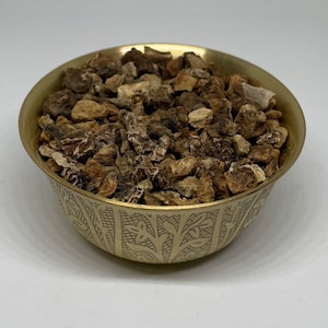 Könnte beinhalten: Eine goldfarbene Schüssel gefüllt mit getrockneten, unregelmäßig geformten Stücken. Die Schüssel hat ein geätztes Design um den Rand. Der Inhalt scheint ein Naturprodukt zu sein, möglicherweise Kräuter oder Wurzeln, mit verschiedenen Braun- und Beigetönen.