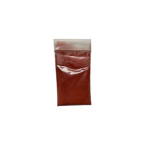 May include: A small, clear plastic bag filled with a vibrant red powder. The bag is sealed at the top with a white strip. The contents are finely ground and fill the bag, creating a solid block of color against a white background.
