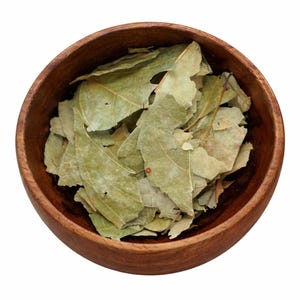 May include: A round, dark brown wooden bowl filled with a collection of dried, light green bay leaves. The leaves are varied in size and shape, showing a matte texture and some natural imperfections, contained within the smooth wooden vessel.