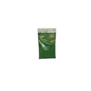 May include: A small, transparent plastic bag containing bright green powder. The bag has a white, sealed top. The contents appear finely ground, suggesting a pigment or cosmetic product. The bag is set against a plain white background.