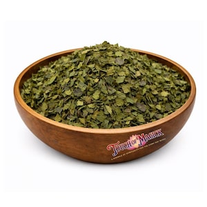 May include: A wooden bowl filled with dried green leaves. The bowl has a natural wood grain finish and is labeled "Touch of Magick". The leaves appear to be finely chopped and have a textured appearance.
