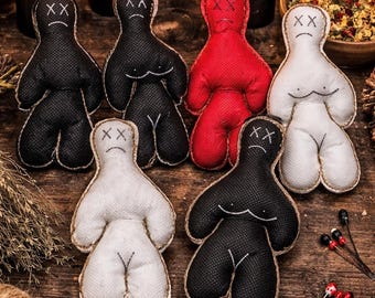 May include: A collection of handmade voodoo dolls in black, red, and white, arranged on a rustic wooden surface. Each doll has stitched facial features and a simple body shape. The scene includes candles, dried herbs, and a skull.
