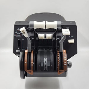 May include: A black flight simulator control panel with two brown gear levers, two white flap levers, and a black flap control knob. The panel has labels for "Gear", "Speed Brake", "Flap", and "Flaps".