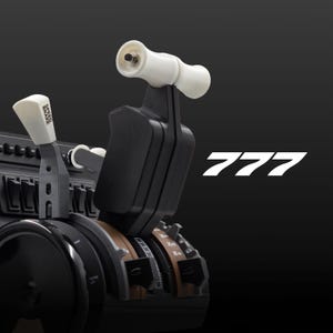 以下が含まれることがあります： 黒と茶色のフライトシミュレーターのコントロールパネル。白いスロットルレバーと黒いスピードブレーキレバーが付いています。パネルには複数のスイッチとノブがあります。テキスト「777」は黒の背景に白で表示されています。