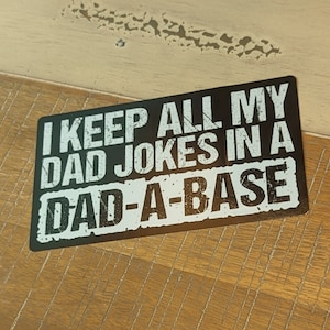 May include: Black metal sign with white text that reads "I keep all my dad jokes in a dad-a-base".