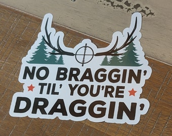 May include: White sticker with a brown antler design and two green pine trees on either side. The text reads "NO BRAGGIN' TIL' YOU'RE DRAGGIN'". There are two red stars on either side of the text.