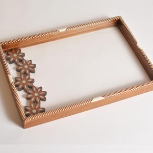 Könnte beinhalten: Ein Holztablett mit einem dekorativen weißen und braunen Rand. Das Tablett hat auf einer Seite ein Blumenmuster.