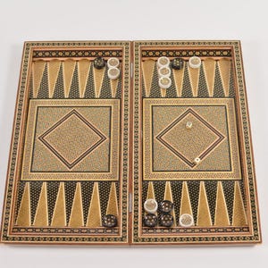 Può includere: Un tabellone da backgammon in legno con intricati disegni intarsiati. Il tabellone è aperto e mostra pedine nere e bianche, nonché dadi.