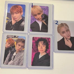 May include: A collection of five trading cards featuring portraits of young people. The cards are encased in clear plastic sleeves. The portraits showcase individuals with various hairstyles and expressions, set against colorful backgrounds.