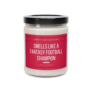 May include: A white candle jar with a red label that says "Smells Like a Fantasy Football Champion" and "Winning Vibes Collection". The jar has a black lid and is 9 oz and burns for 50 hours.