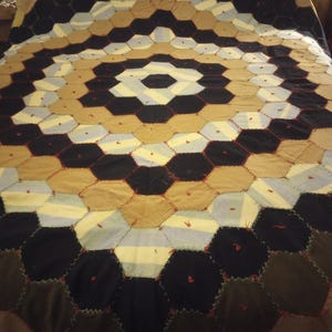 May include: A large, circular quilt made of various fabric scraps in shades of brown, black, white, and blue. The quilt is sewn in a hexagonal pattern, creating a visually appealing geometric design.