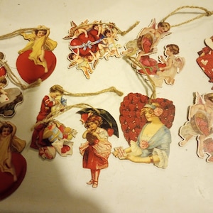 May include: A collection of vintage-style Valentine's Day ornaments. The ornaments feature cherubs, hearts, and figures in red, yellow, and white. Each ornament has a twine loop for hanging. The overall theme is romantic and nostalgic.
