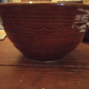 May include: A brown ceramic mixing bowl with a white design. The bowl has a wavy pattern around the top and a star-shaped design on the side.