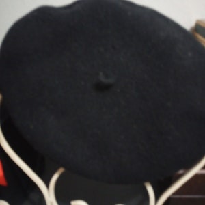 May include: A black beret hat on a white metal display stand.